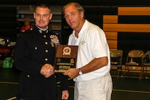 Maj. Christopher L. Buck, Recruiting Station Lansing commanding officer, left, presents Ron Stremlow, Forest Area High School coach, with the Recruiting Station Lansing High School Coach of the Year Award inside the Forest Area High School gymnasium, Oct. 8, 2015. Ron Stremlow coached volleyball, girls and boys soccer and basketball, track, football, and middle school basketball. Each year, RS Lansing solicits nominations from high schools throughout Michigan and recognizes one male and one female coach that exemplifies the Marine Corps values of honor, courage and commitment.