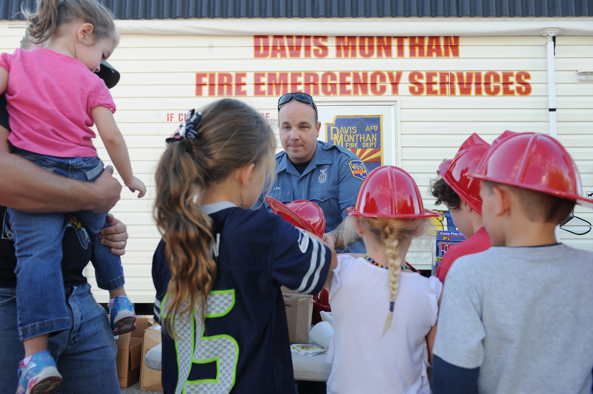 U.S. Air Force Jason Rice, 355th Civil Engineering Squadron Fire and Emergencies Services unit captain, passes out helmets and pamphlets to local children during a National Night Out event at Davis-Monthan Air Force Base, Ariz., Oct. 7, 2015. The event is intended to educate the public about crime and drug prevention as well as strengthen neighborhood spirit and security-organization. Rice gave children and parents different items that would help teach them this in a fun way. (U.S. Air Force photo by Senior Airman Cheyenne A. Powers/Released) 