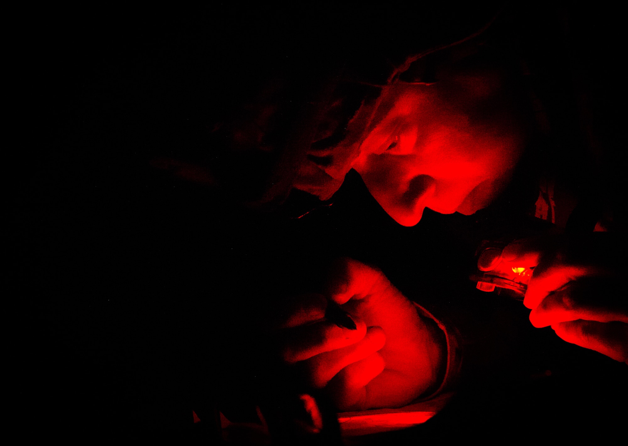 Lt. Col. Erin Hutchinson, 446th Aeromedical Staging Squadron Expert Field Medic Badge candidate, plots points on a map under a tarp during the rain while being restricted to only using a red light flashlight before the night land navigation test during the EFMB course at Joint Base Lewis-McChord, Wash., Sept. 25, 2015. Every year airmen and soldiers attempt to pass the EFMB course where less than 20 percent of all candidates leave successful. (U.S. Air Force photo by Senior Airman Jordan Castelan/Released)