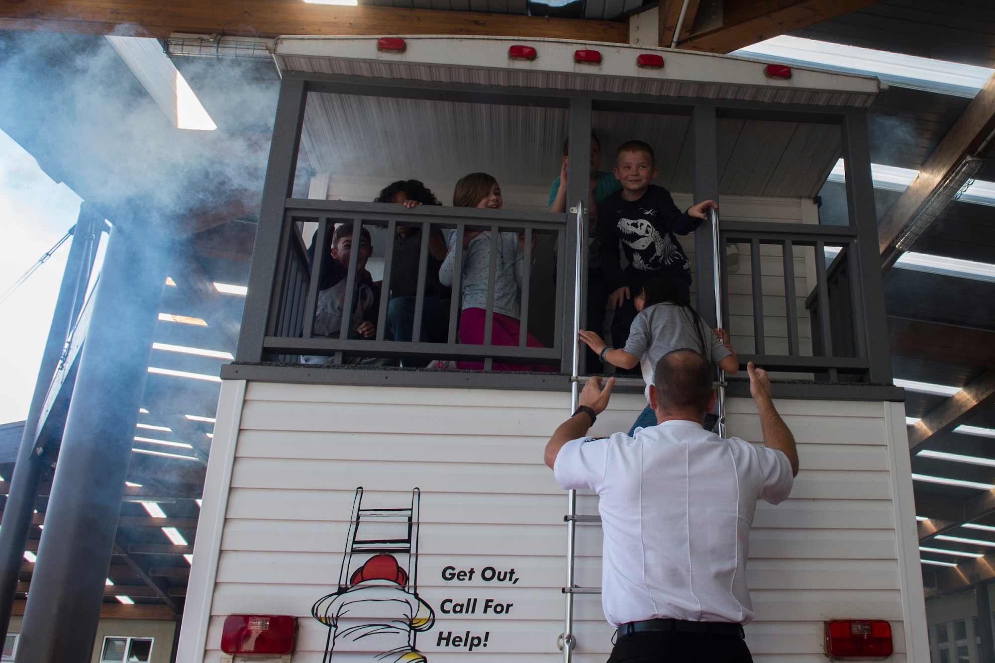 Ingo Alf, a 52nd Civil Engineer Squadron fire inspector, helps Bitburg Elementary School students down a ladder while practicing exiting a building during a visit from the Spangdahlem Fire Department at BES on Bitburg Annex, Germany, Oct. 8, 2015. The pretend house fire taught the students to check if doors are warm with the back of their hands and to call for help once you are out of the house. (U.S. Air Force photo by Airman 1st Class Luke J. Kitterman/Released)