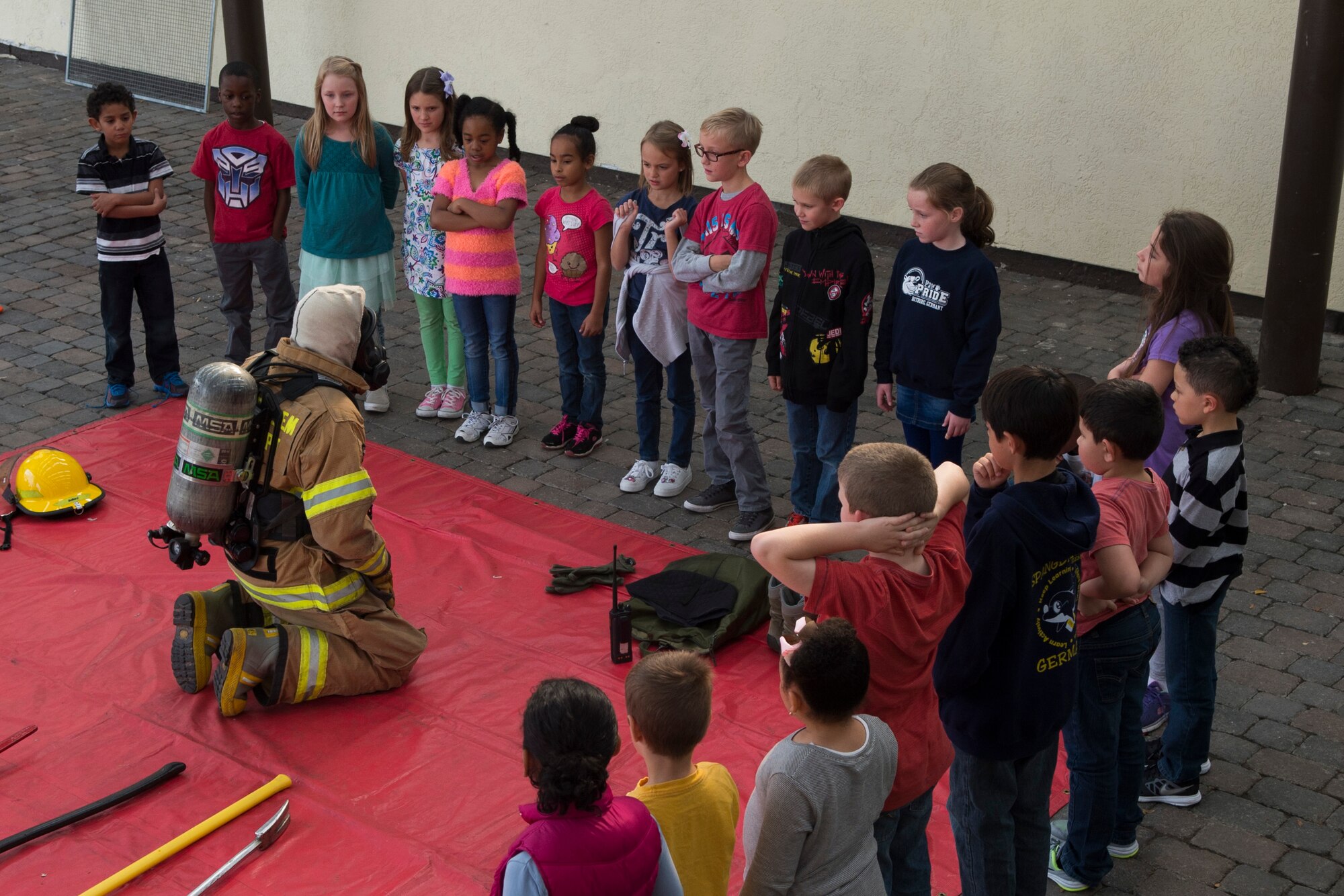 U.S. Air Force Airman 1st Class Ty Hults, a 52nd Civil Engineer Squadron firefighter, shows Bitburg Elementary School students firefighter equipment while visiting BES on Bitburg Annex, Germany, Oct. 8, 2015. U.S. Air Force Col. Joe McFall, 52nd Fighter Wing commander, proclaimed Oct. 4-10 as Fire Prevention Week which included school visits and fire-safety demonstrations in front of the Exchange by the Spangdahlem Fire Department. (U.S. Air Force photo by Airman 1st Class Luke J. Kitterman/Released)