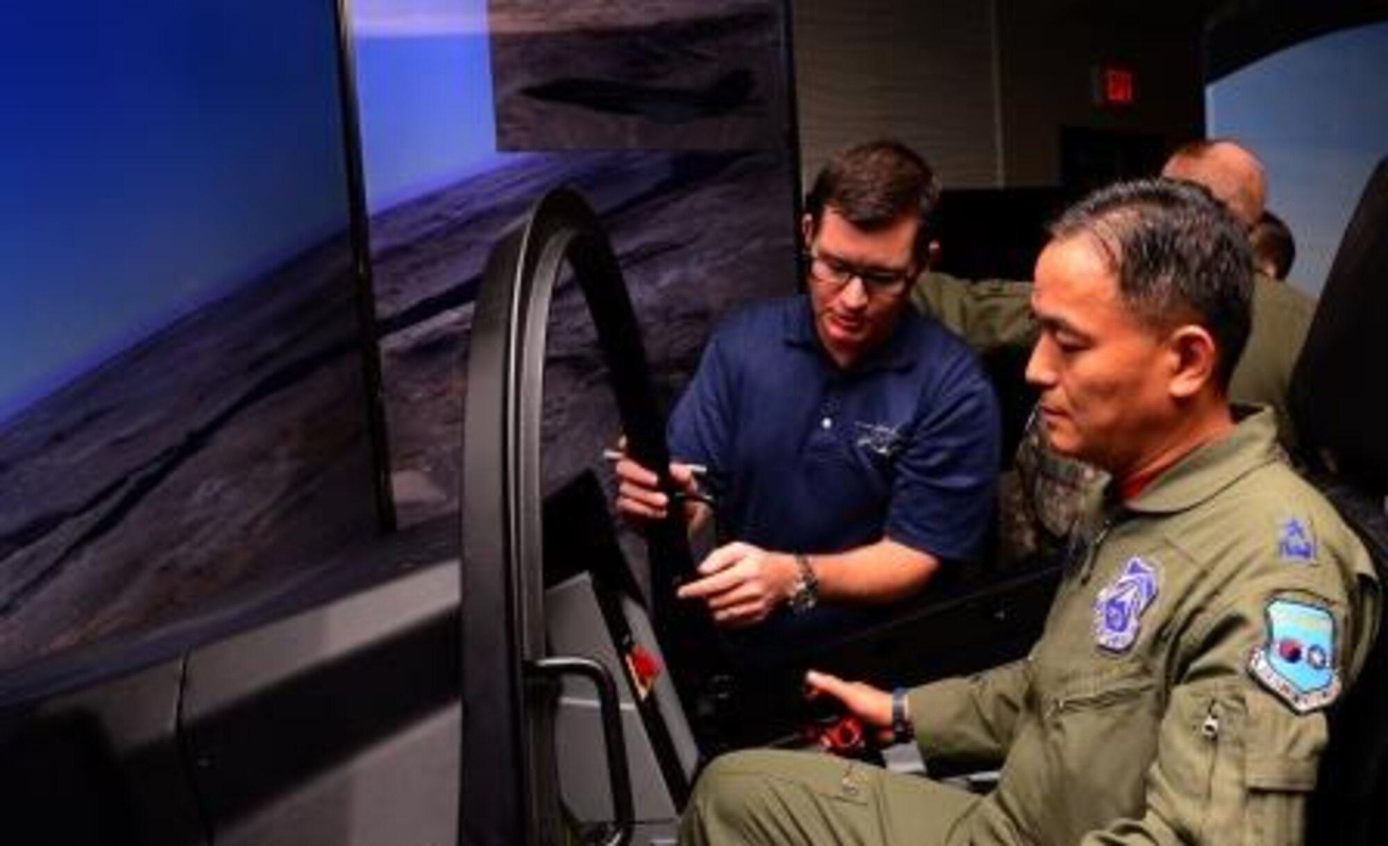 Republic of Korea Air Force Brigade General Duk-gu Cho, Korean Air Operations Center director, flies the F-35 Lightning II demonstrator with assistance from Lockheed Martin simulator instructor Matt Cliver Oct. 8, 2015, at Osan Air Base, Republic of Korea. Both ROKAF and United States Air Force members took the chance to fly the simulator throughout the day. (U.S. Air Force photo by Staff Sgt. Benjamin Sutton) 