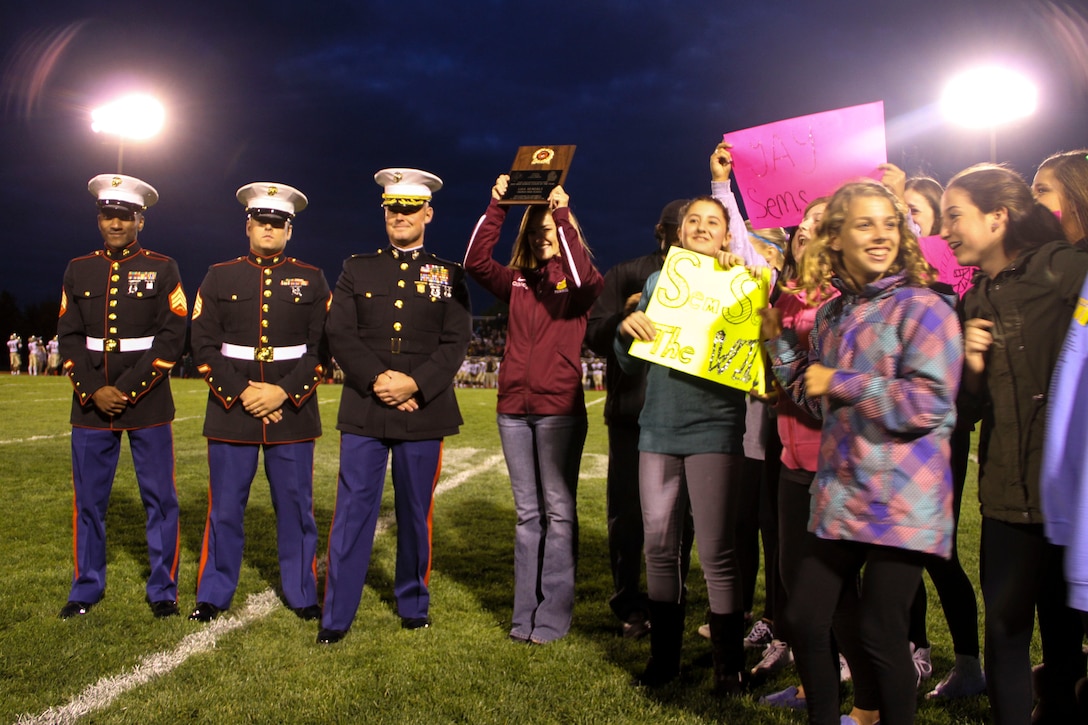 Maj. Christopher L. Buck, Recruiting Station Lansing commanding officer, third from left, presents Lisa Semerly, Okemos High School coach, with the Recruiting Station Lansing High School Coach of the Year Award inside on the Okemos football field, Oct. 9, 2015. Each year, RS Lansing solicits nominations from high schools throughout Michigan and recognizes one male and one female coach that exemplifies the Marine Corps values of honor, courage and commitment.