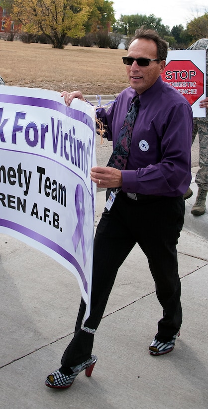 Glenn Garcia, 90th Medical Group Family Advocate, walks in a pair of high-heels while carrying a “We walk for the victims” banner Oct. 9, 2015, during a domestic violence walk on F.E. Warren Air Force Base, Wyo. The idea of walking a mile in their shoes helps individuals understand the perspective of others. (U.S. Air Force photo by Senior Airman Brandon Valle)