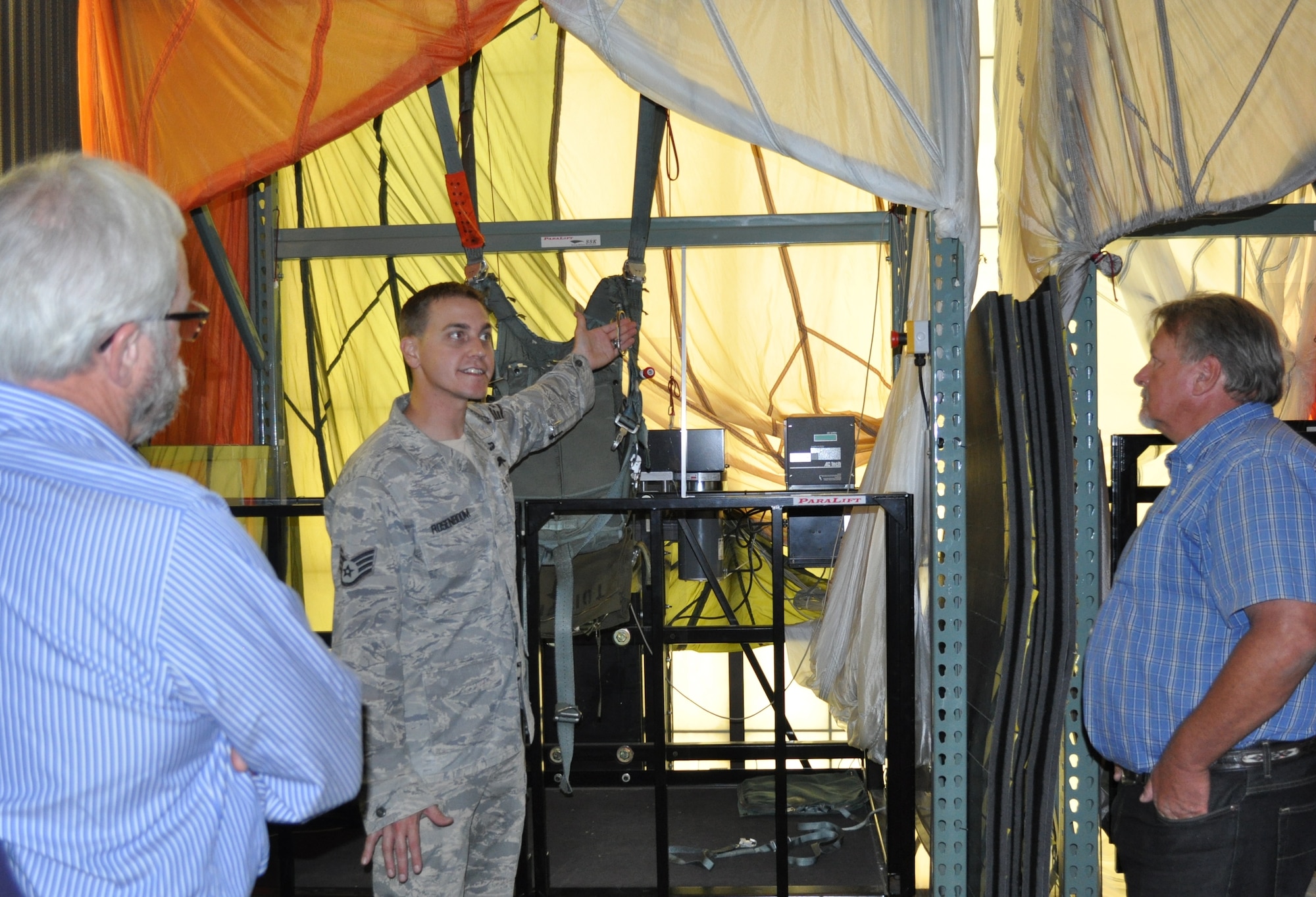 Staff Sgt. Mark Rosenboom points out features of a parachute to civic leaders  Scott Farmer, left, and  Jack Caldwell, right. Rosenboom is a Survival, Evasion, Resistance and Escape instructor for the 60th Operations Support Squadron. (U. S. Air Force photo/Ellen Hatfield)
