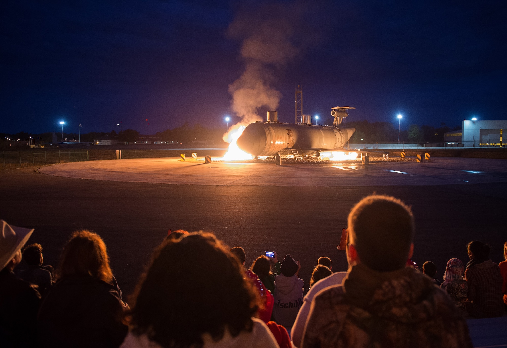 Attendees of an open house watch as a fire-training aircraft burns Oct. 8, 2015, at Ramstein Air Base, Germany. The event was hosted by the 86th Civil Engineer Squadron to promote Fire Prevention Week. During the open house, attendees were able to receive different information about fire safety including home-fire safety issues, fire extinguisher training and holiday safety tips. The event concluded with a live-fire demonstration, where leadership from throughout Ramstein helped firefighters extinguish a simulated aircraft fire in the burn pit. (U.S. Air Force photo/Senior Airman Damon Kasberg)