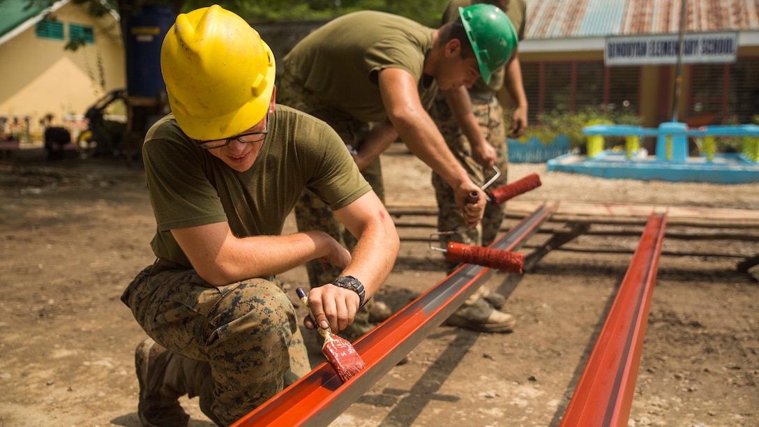 U.S. service members work together to paint metal beams while working on the humanitarian civic assistance project at Binduyan Elementary School Sept. 30, during Amphibious Landing Exercise 2015. PHIBLEX 15 is an annual, bilateral training exercise conducted by members of the Armed Forces of the Philippines alongside U.S. Marine and Navy Forces. It focuses on strengthening the partnership and relationships between the two nations across a range of military operations, including disaster relief and complex expeditionary operations. the metal will be used to make an overhang for the school. The service members are with 9th Engineer Support Battalion, 3rd Marine Logistics Group, III Marine Expeditionary Force. 