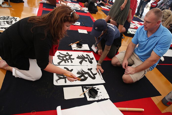 Gunnery Sgt. Victor Mancini, maintenance control staff non-commissioned officer with Marine Aerial Refueler Transport Squadron 152, aboard Marine Corps Air Station Iwakuni, Japan (right), and his wife, Arlene Mancini (left), compete against Japanese locals in a calligraphy contest during a cultural adaption program trip to the annual Japanese Calligraphy Brush Festival, in Kumano, Hiroshima Prefecture, Sept. 23, 2015. This cultural trip is one of many events coordinated to assist service members and their families adapt to the Japanese lifestyle.