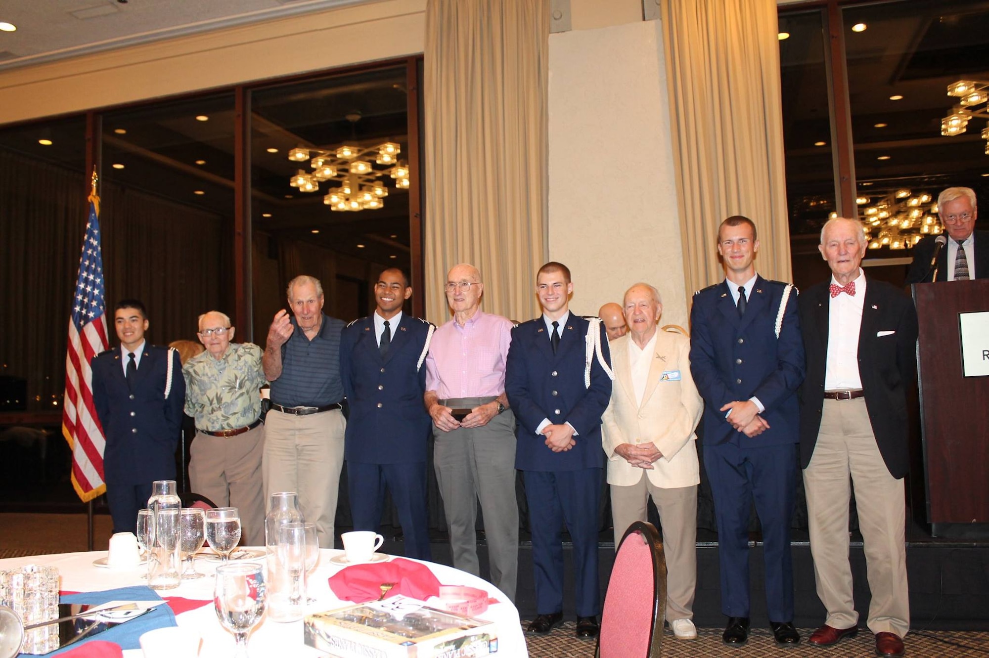 Veterans of the 6th Bomb Group stand with AFROTC cadets from the color guard of the University of Portland’s AFROTC Det 695, after the reunion banquet on 12 September 2015 in Portland, Oregon.  From left to right are C/Capt Collin Whitney, Dick Randall, Ed Vincent, C/3C Jacob San Agustin, Virgil Morgan, C/Capt Joseph Baumann, Bob Frick, C/Capt Samuel DeWhitt and Warren Higgins.  The 6th BG Association President, John Creek, Jr., looks on from the podium.  (Courtesy Mr. Philip Conroy)