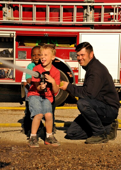 Children from the Grand Forks Air Force Base Youth Center hold and spray a fire hose while a member of the 319th Civil Engineer Squadron fire department helps guide them during a fire prevention activity Oct. 7, 2015, on Grand Forks AFB, North Dakota. The fire department, hosted multiple fire prevention events to emphasize the importance of fire safety. (U.S. Air Force photo by Senior Airman Xavier Navarro/Released) 