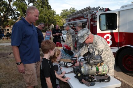 Tech. Sgt. Joseph Tvrdy (right), 502nd Civil Engineer Squadron firefighter, describes the use of fire gear to Mark Teusch (left), and his children Alexander and Sarah during the National Night Out Oct. 6 at Joint Base San Antonio-Randolph.