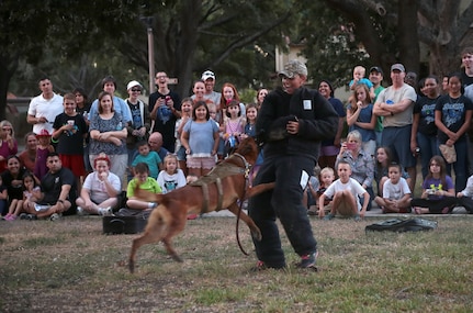 Airman 1st Class Victoria Dunning, 902nd Security Forces Squadron electronic security systems manager, demonstrates the attack capabilities of a military working dog during National Night Out Oct. 6 at Joint Base San Antonio-Randolph. Hosted in a block party atmosphere, National Night Out provides an opportunity each year for JBSA-Randolph community members to interact with each other and first responders and to learn about various base agencies.
