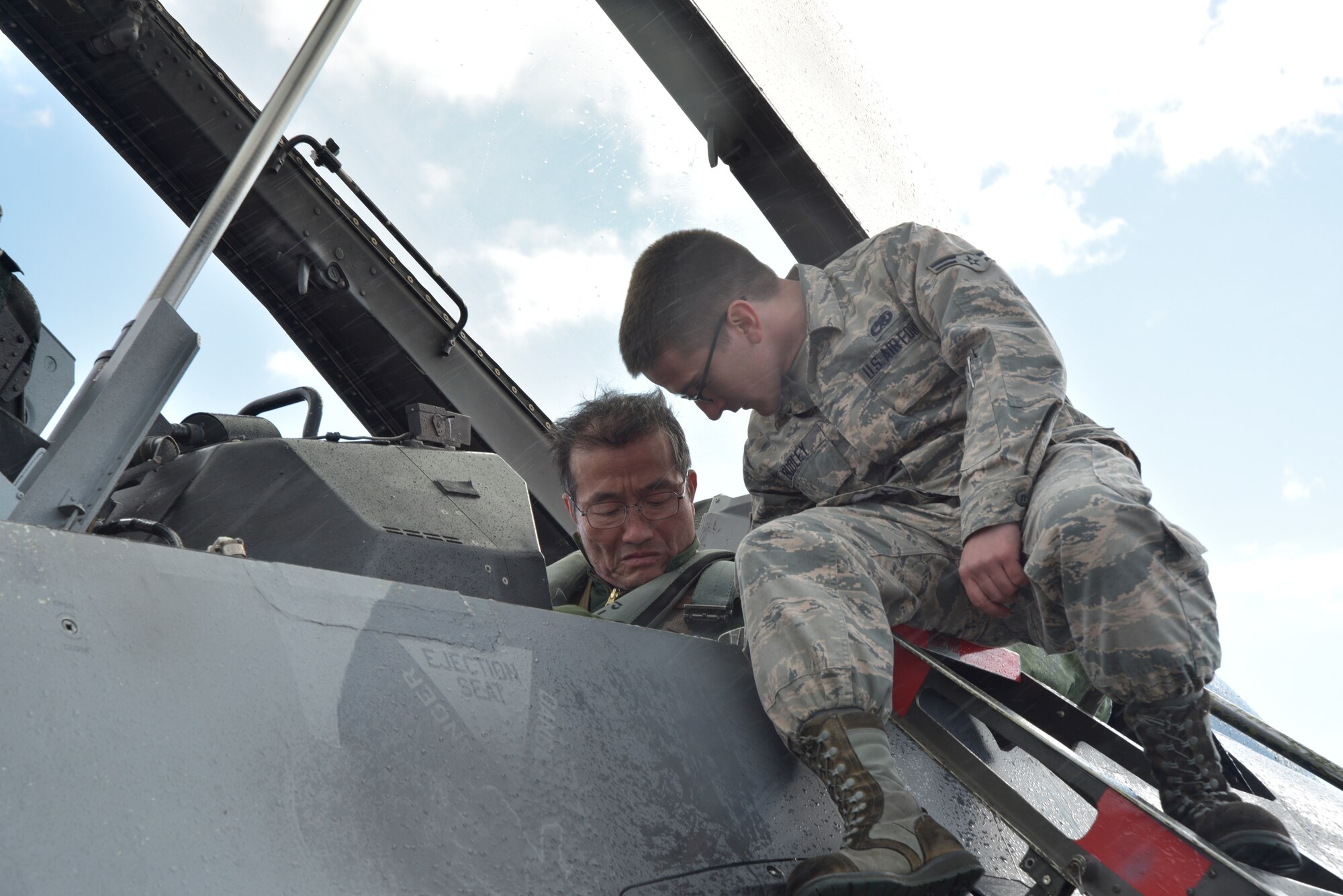 U.S. Air Force Airman 1st Class Jacob Dudley, 35th Aircraft Maintenance Squadron crew chief, secures a strap on a seat for Japan Air Self-Defense Force Lt. Gen. Yoshiyuki Sugiyama, Air Defense Command commander, at Misawa Air Base, Japan, Oct. 14, 2015. Sugiyama was preparing to fly in an F-16 Fighting Falcon as part of a bilateral exchange flight with the 13th Fighter Squadron. (U.S. Air Force photo by Senior Airman Jose L. Hernandez-Domitilo/Released)