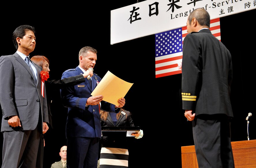 U.S. Air Force Brig. Gen. Barry Cornish, 18th Wing commander, reads a certificate of commendation to Mitsuo Yamaguchi, 18th Civil Engineer Squadron fire training section assistant, on behalf of the Kadena Air Base local employees during a joint Length of Service Award ceremony at the Okinawa Convention Center in Ginowan City, Japan, Oct. 15, 2015. A total of 265 local employees from Kadena were awarded the Joint Length of Service Award. (U.S. Air Force photo by Naoto Anazawa)