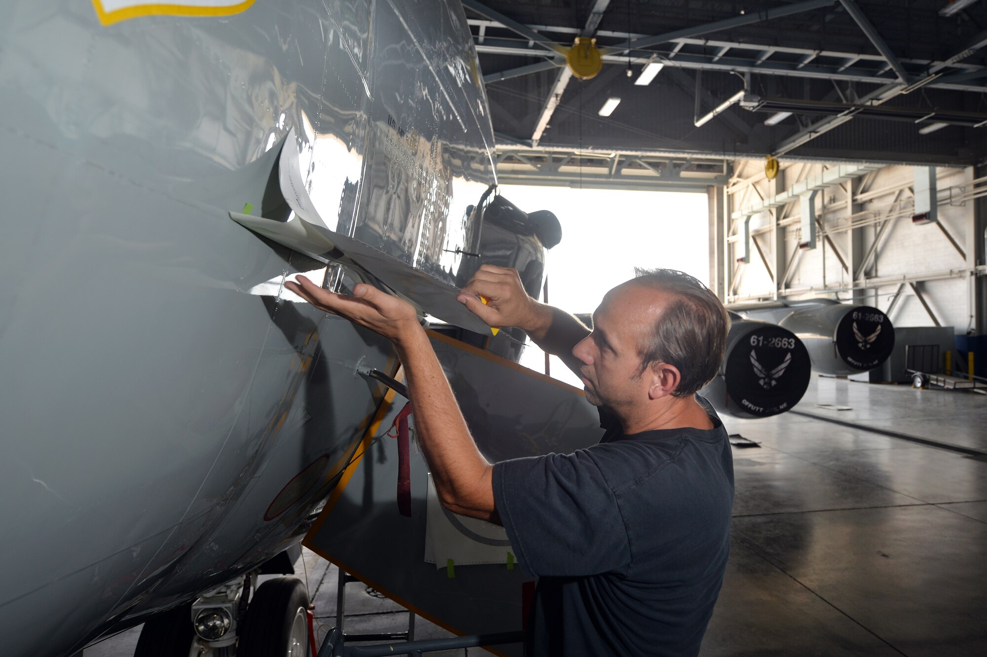 James Battig, a fabrication work leader with the 55th Maintenance Squadron, carefully reveals the inaugural piece of nose art that on an RC-135S Cobra Ball aircraft on Sept. 2, Offutt Air Force Base, Neb.  Members of the 55th Maintenance squadron are responsible for commissioning the art pieces that will grace the noses of the RC fleet.  (U.S. Air Force Photo by Josh Plueger/Released)