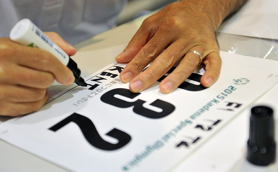 Hiroshi Higa, 18th Contracting Squadron master labor contract specialist, writes a Kadena Special Olympics athlete's name on a sport bib in preparation for KSO at the Schilling Community Center on Kadena Air Base, Japan, Oct. 16, 2015. This is the 16th annual KSO, a sporting event dedicated to enriching the lives of special-needs individuals while strengthening Okinawa- U.S.  relations. (U.S. Air Force photo by Naoto Anazawa)
