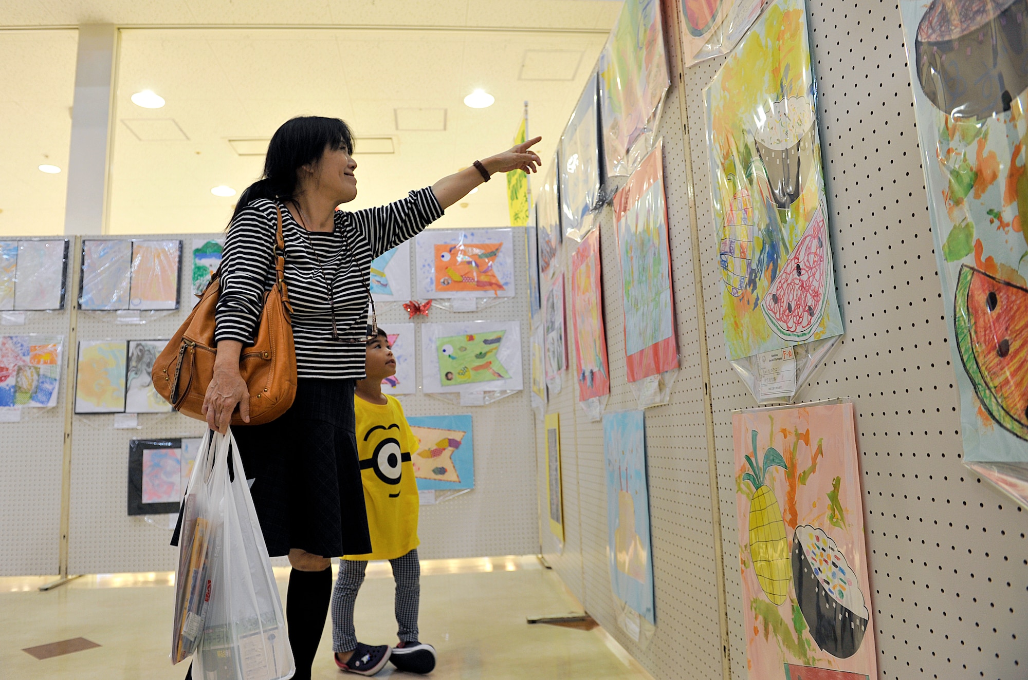 A guest shows artwork to her grandchild during the Kadena Special Olympics Art Exhibit at Main City Shopping Mall San-A in Uruma City, Oct. 16, 2015. The art exhibit is part of KSO and is held to showcase the talent and effort of special needs children from the local community. The art work from the exhibit will be displayed during KSO Nov. 7, on Kadena Air Base. (U.S. Air Force photo by Naoto Anazawa)