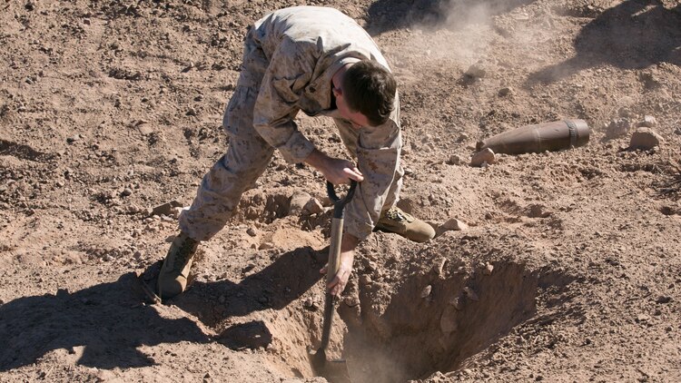 Sgt. Brendan Campbell, on-the-job trainee, Explosive Ordnance Disposal, digs out loose dirt from a hole created from an M2A4 shaped charge at Rainbow Canyon Training Area, Oct. 8, 2015. The first day of the excavation was used as training for EOD while also helping the Natural Resources and Environmental Affairs Division create a water source for wildlife aboard the Combat Center. 