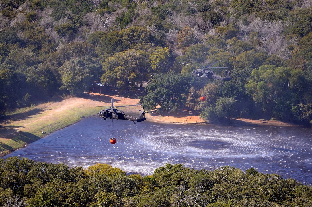 Two Texas Army National Guard UH-60 Black Hawk helicopters refill their firefighting buckets in a lake before continuing to battle wildfires threatening homes and property near Bastrop, Texas, Oct. 14, 2015. Texas Air National Guard photo by 1st Lt. Alicia Lacy