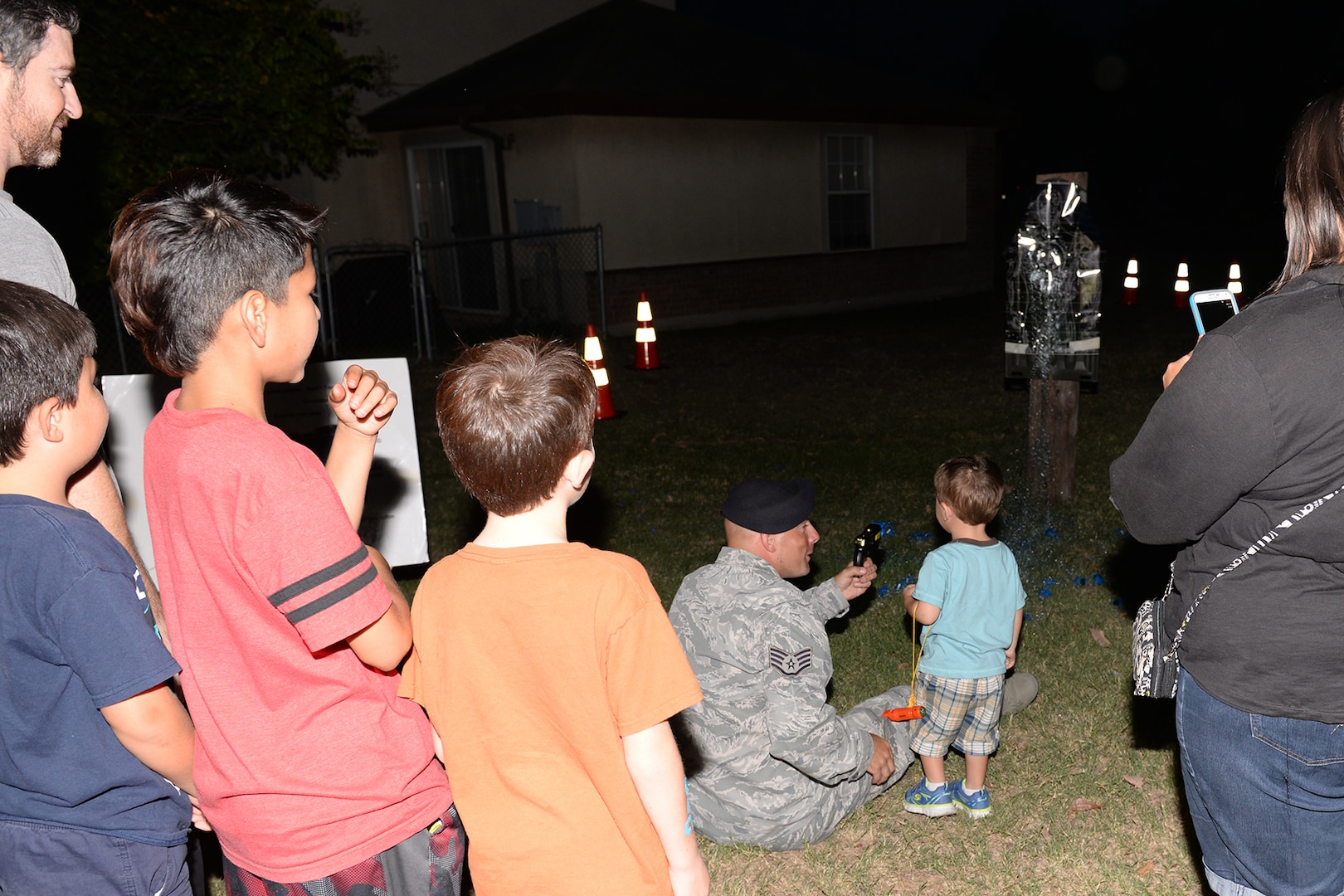Staff Sgt. Scott Aberle, 802nd Security Forces Squadron training instructor, assists children in safely using a Taser to shoot a target during National Night Out Oct. 6, 2015, at Joint Base San Antonio-Lackland, Texas. The one of the purposes of the annual event is to enhance relations between the police and community, and increase neighborhood camaraderie. (U.S. Air Force photo by Senior Airman Krystal Wright/Released)