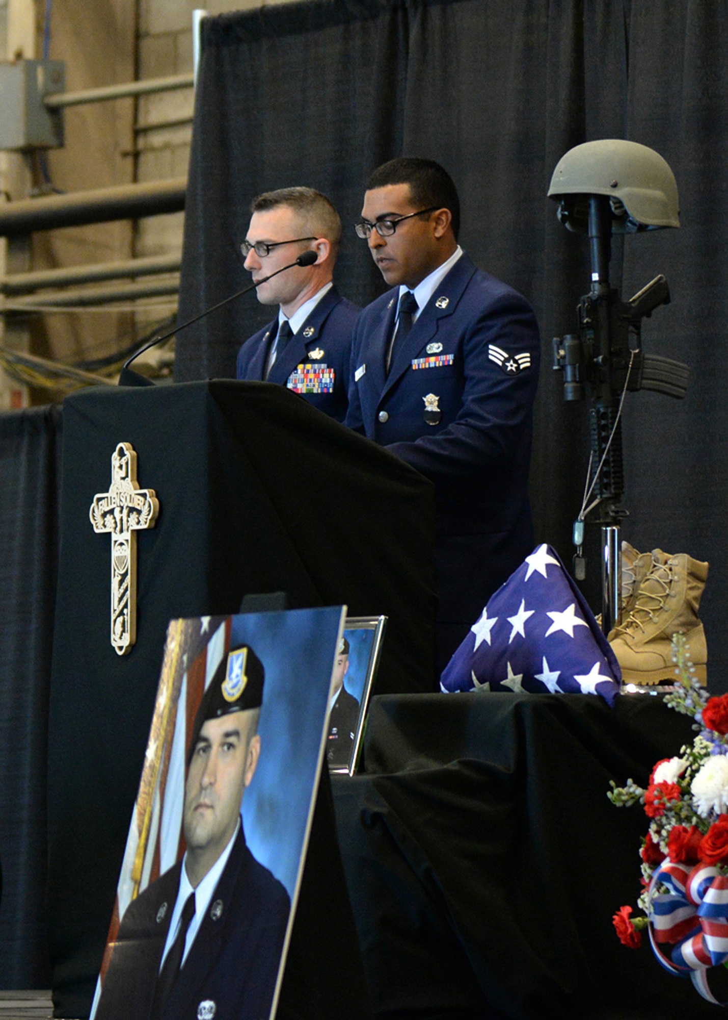 Senior Airman Wilyaveh Cruz-Santiago (right) reads Senior Airman Nathan Sartain's biography during a memorial service for Sartain and Senior Airman Kcey Ruiz at the Aero Club Hangar at Hanscom Air Force Base, Mass., Oct. 16, while Staff Sgt. Lee Shortell looks on. At the service, colleagues remembered the two fallen security forces Airmen, who were killed Oct. 2, when the C-130J Super Hercules they were on crashed shortly after takeoff from Jalalabad, Afghanistan. (U.S. Air Force photo/)