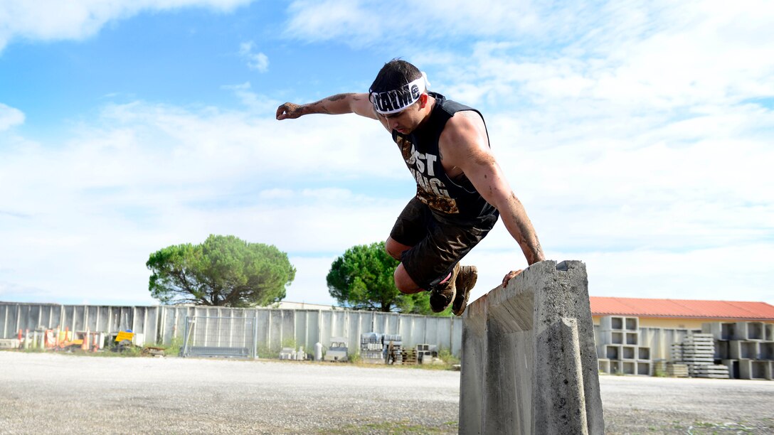 U.S. Air Force Senior Airman Cameron Flint, 31st Maintenance Squadron aerospace ground equipment technician, jumps over a T-wall during the Wyvern Mud Run, Oct. 17, 2015, at Aviano Air Base, Italy. The Wing Diversity Council and 31st Civil Engineer Squadron hosted the event, which awarded prizes to the top male and female, top team and top squadron team. (U.S. Air Force photo by Senior Airman Areca T. Bell/Released)