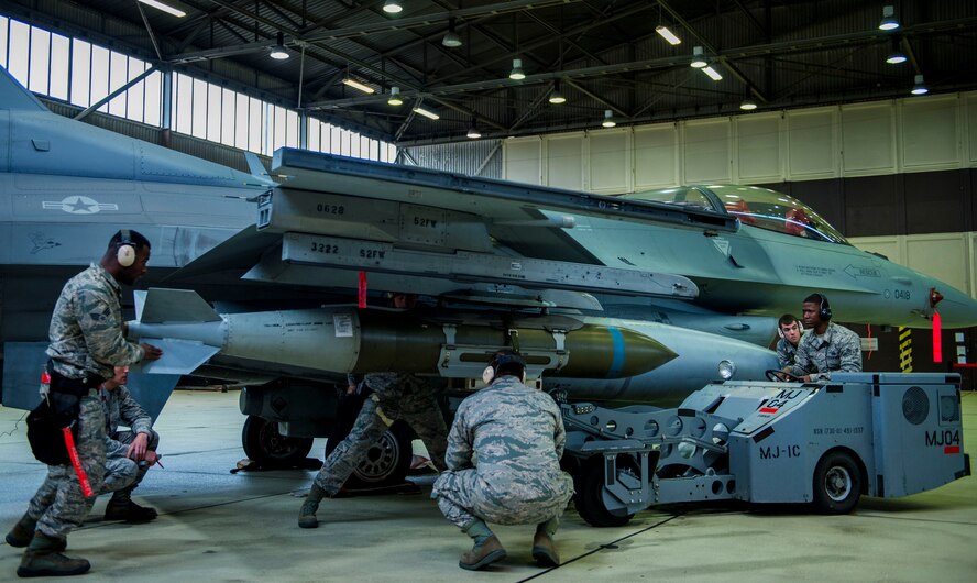 Members of one of the load competition teams work to load a dummy weapon on to an F-16 Fighting Falcon fighter aircraft during the quarterly weapons load competition in Hangar 1 on Spangdahlem Air Base, Germany, Oct. 16, 2015. Family, friends and members of the Spangdahlem community attended the competition to see which of the two teams of three maintenance Airmen would move on to the annual load competition. U.S. Air Force Col. Joe McFall, 52nd Fighter Wing commander, U.S. Air Force Chief Master Sgt. Brian Gates, 52nd Fighter Wing command chief, and U.S. Air Force Col. Stephen Scherzer, 52nd Maintenance Group commander, attended the competition and congratulated the winning team afterwards.