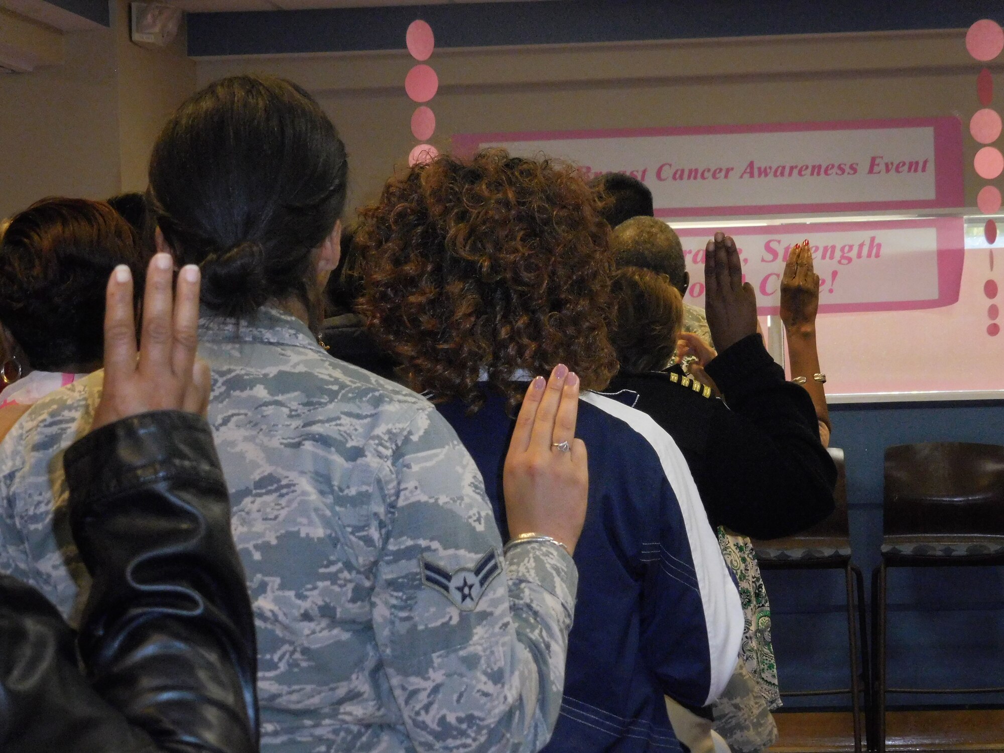 Approximately 60 attendees stood up, raised their hands, and took a pledge to fight breast cancer at a Breast Cancer Awareness event  on Oct. 16 at Malcolm Grow Medical Clinics and Surgery Center.  The purpose of the event was to help educate patients and staff about breast cancer and the importance of early detection and prevention and to offer comfort and support to those diagnosed or undergoing treatment.  (Photo by Kathy Canfield)
