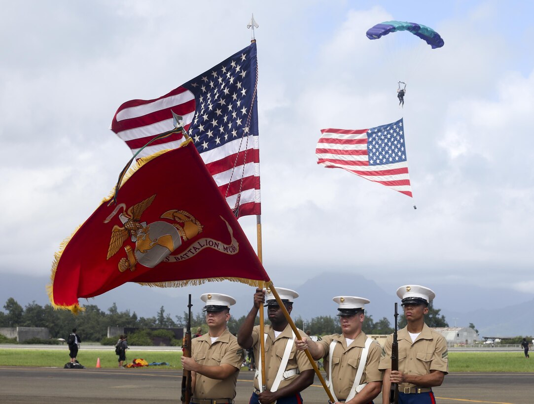 The Marine Corps Base Hawaii Color Guard presents the colors during the national anthem as a parachutist from the Flying Leathernecks, a civilian skydiving organization, descends with the U.S. flag to begin the 2015 Kaneohe Bay Air Show at Marine Corps Base Hawaii, Oct. 18, 2015. U.S. Marine Corps photo by Cpl. Ricky S. Gomez