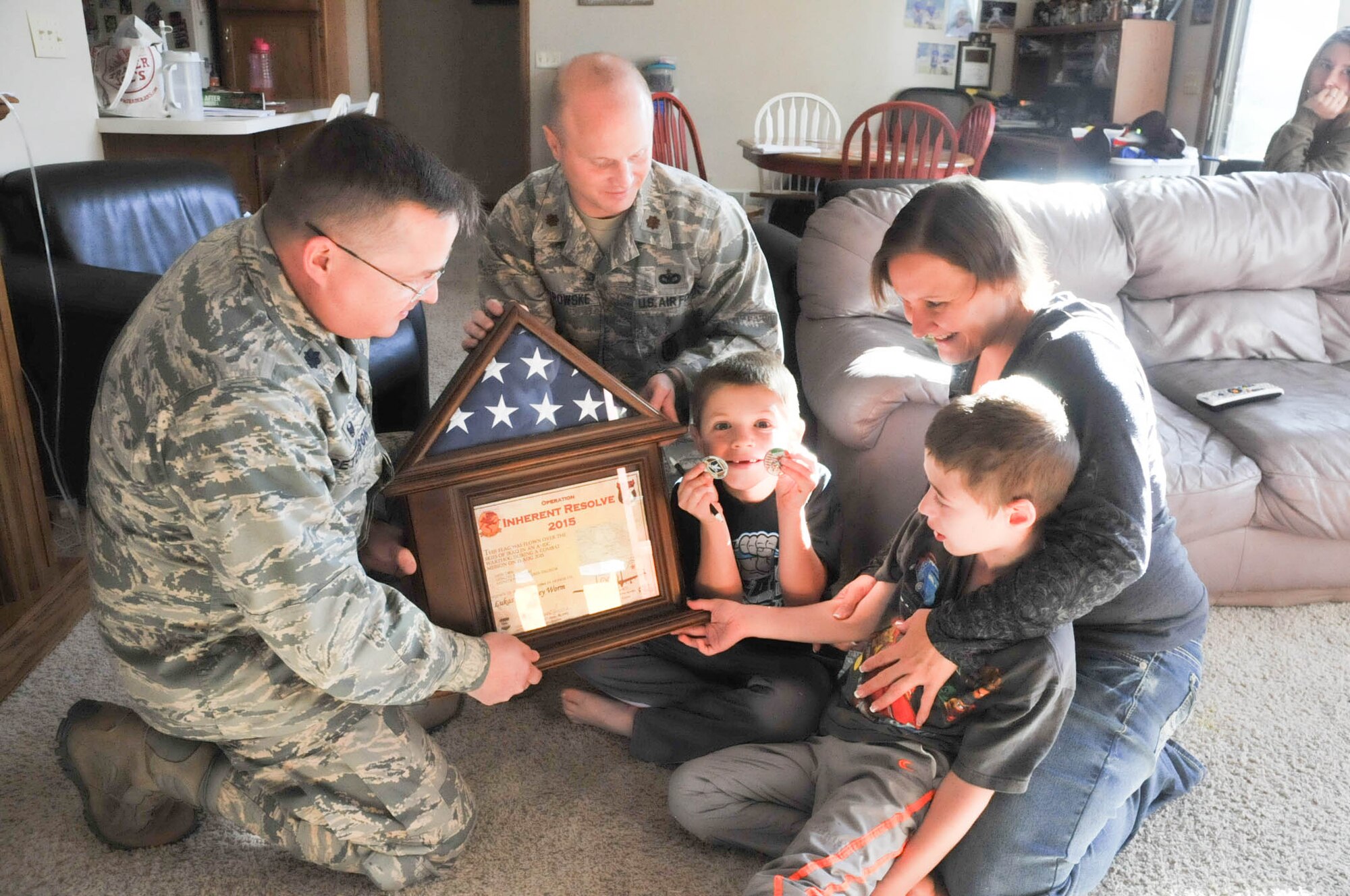 Lt. Col. Greg Peterson and Maj. Judd Citrowske, 934th Security Forces Squadron, present Lukas Worm (seated with mother Nadine) with a US flag flown on an A-10 mission during Operation Inherent Resolve. Lukas' family is friends with Tech. Sgt. Chuck Smizek, 934th SFS, who arranged for the flag to be delivered to Lukas who has a degenerative brain disorder. Lukas' brother Isaac displays the squadron and A10 coins that were also presented along with the flag. (Air Force Photo/Master Sgt. Justin Siebenahler/Released)