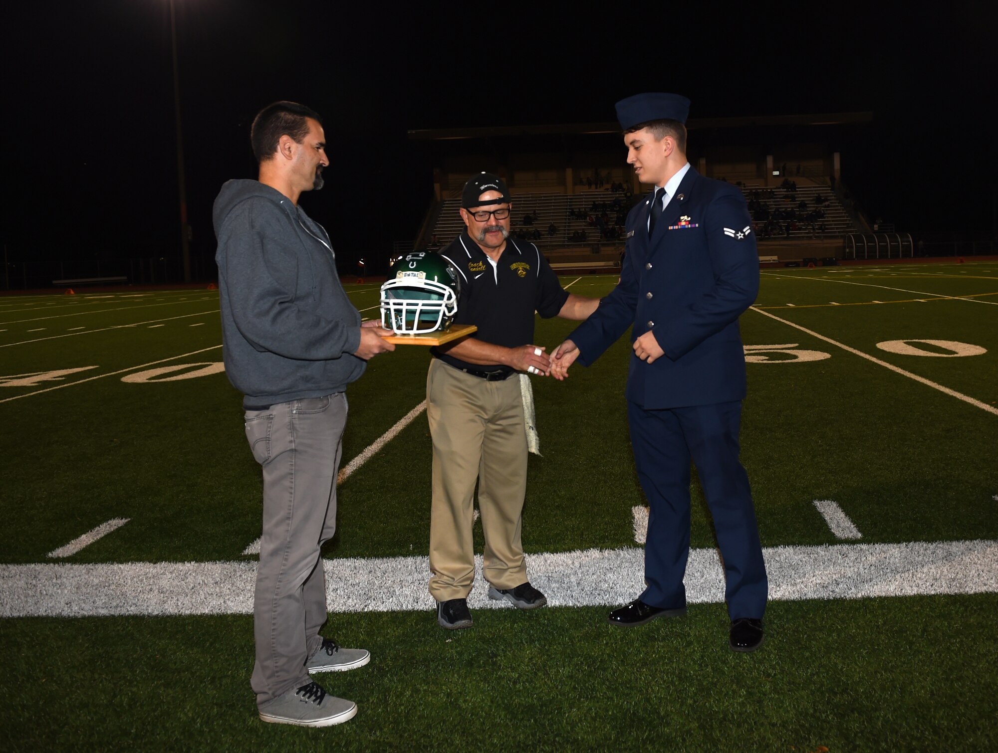 Russ Hohn, Clover Park booster club member (left), and John Randall, Clover Park High School football coach (middle) present Senior Airman Zachary Schroeder, 62nd Aircraft Maintenance Squadron communication navigation mission system journeyman, a plaque from the Clover Park High School Warrior Football team on Warrior Night, Oct. 16, 2015 in Lakewood, Wash. The Warriors honored three McChord Airmen to show gratitude for their selfless service. (U.S. Air Force photo/Senior Airman Naomi Griego)