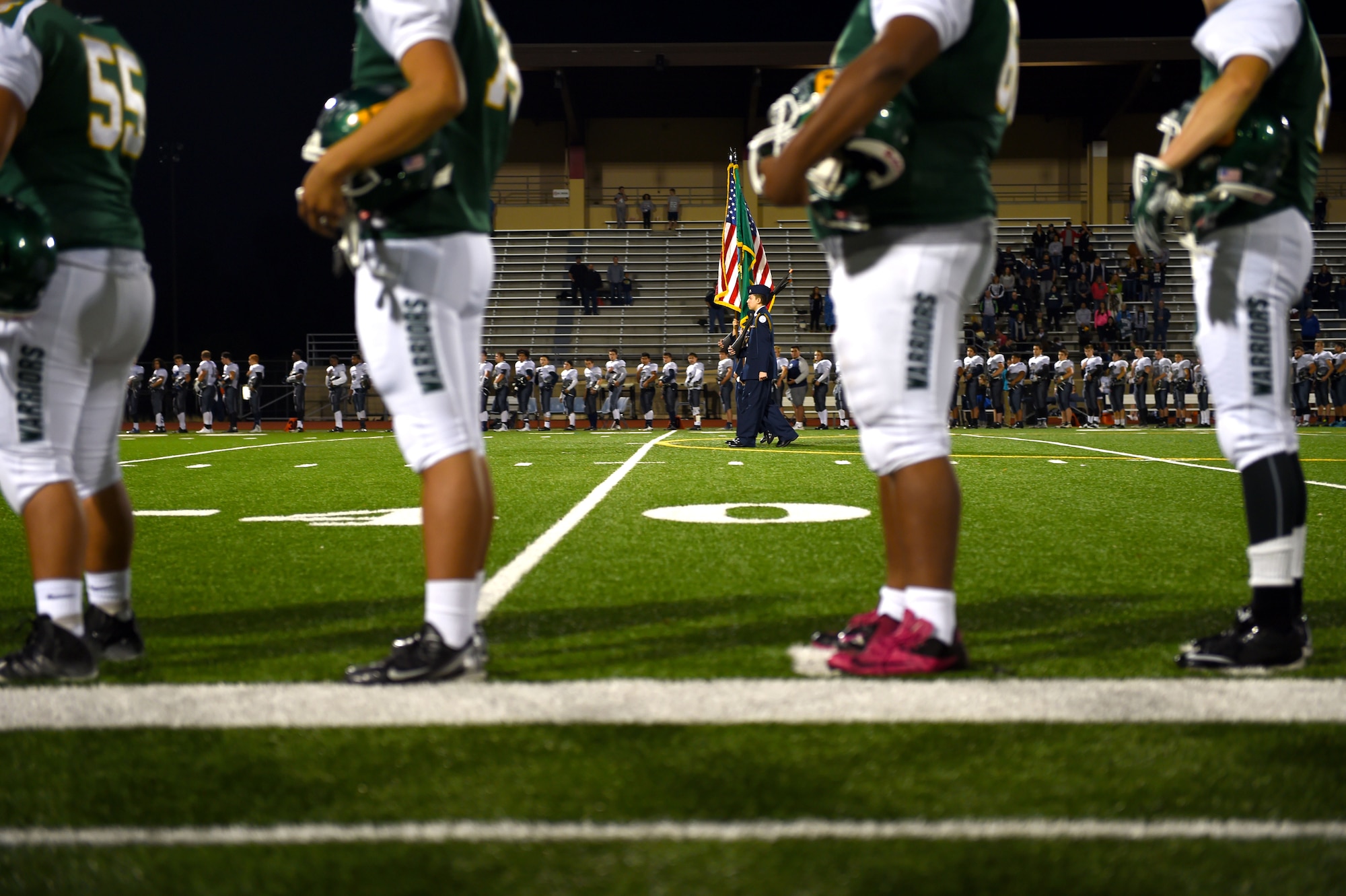 Clover Park and River Ridge High School football players line the field during the presentation of colors and National Anthem prior to the start of their football game and Warrior Night Oct. 16, 2015 in Lakewood, Wash. Three McChord Airmen were invited to be honored during Warrior night for their selflessness and service to others.(U.S. Air Force photo/Senior Airman Naomi Griego)