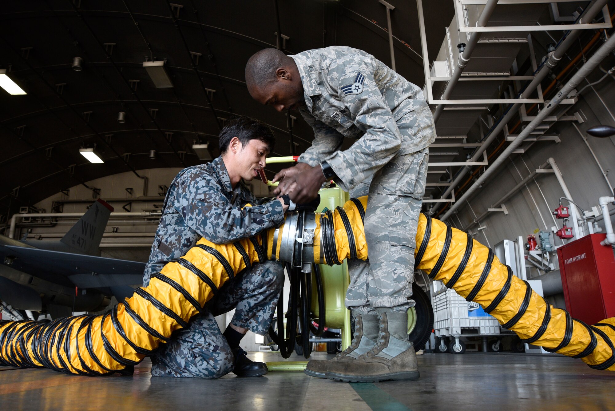 U.S. Air Force Senior Airman Revel Bellamy, 35th Aircraft Maintenance Squadron avionics journeyman, assists Japan Air Self-Defense Force Staff Sgt. Yuuichi Sato, in connecting air flow hoses at Misawa Air Base, Japan, Oct. 1, 2015. The hoses were part of a portable air conditioning unit that cooled an F-16 Fighting Falcon aircraft while troubleshooting was done on the cockpit. (U.S. Air Force photo by Senior Airman Jose L. Hernandez-Domitilo/Released)