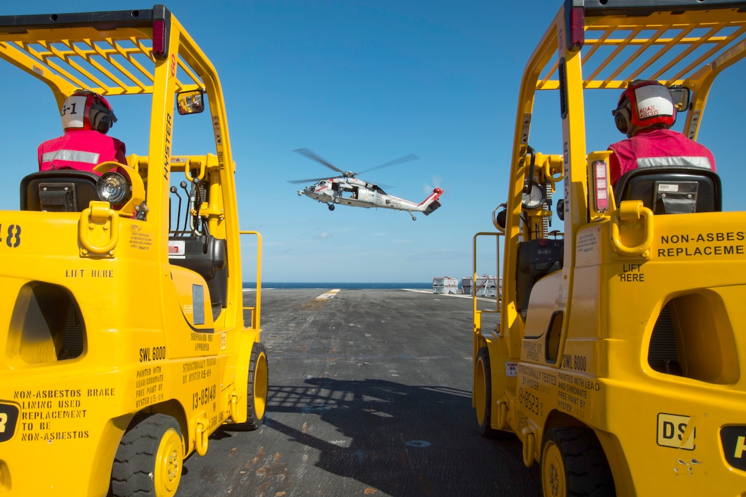 U.S. sailors operating forklifts stand by as an MH-60S Sea Hawk helicopter delivers ammunition to the aircraft carrier USS Dwight D. Eisenhower in the Atlantic Ocean, Oct. 13, 2015. The supplies came from dry cargo and ammunition ship USNS Robert E. Peary during an ammunition replenishment. U.S. Navy photo by Seaman Anderson W. Branch