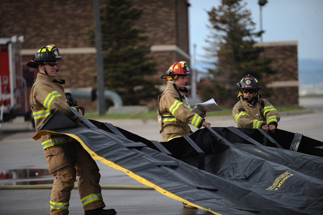 Senior Airman Jordan Lapoint, left, Staff Sgt. Matthew Wright, center, and Senior Airman Joshua Cristi, right, 28th Civil Engineer Squadron firefighters, work together to spread out a decontamination line mat during a hazardous material training exercise at Ellsworth Air Force Base, S.D., Oct. 9, 2015. The DECON line is used to sterilize responders to prevent any dangerous materials being brought back to non-contaminated zones. (U.S. Air Force photo by Airman Sadie Colbert/Released)
