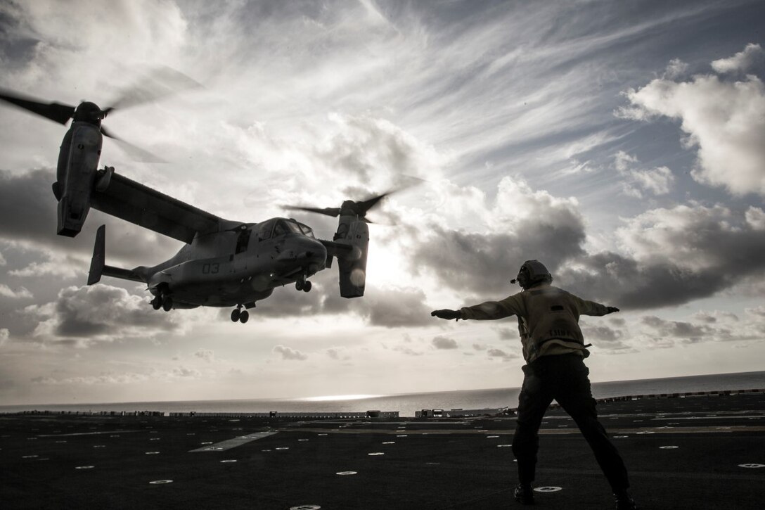 A flight crew member guides a Marine Corps MV-22 Osprey as it approaches the flight deck of the USS Boxer while at sea, Oct. 19, 2015. Marines with Marine Medium Tilt Rotor Squadron 166 Reinforced, the air-combat element of the 13th Marine Expeditionary Unit, land and stow aircraft in preparation for an upcoming tour abroad. U.S. Marine Corps photo by Cpl. Briauna Birl