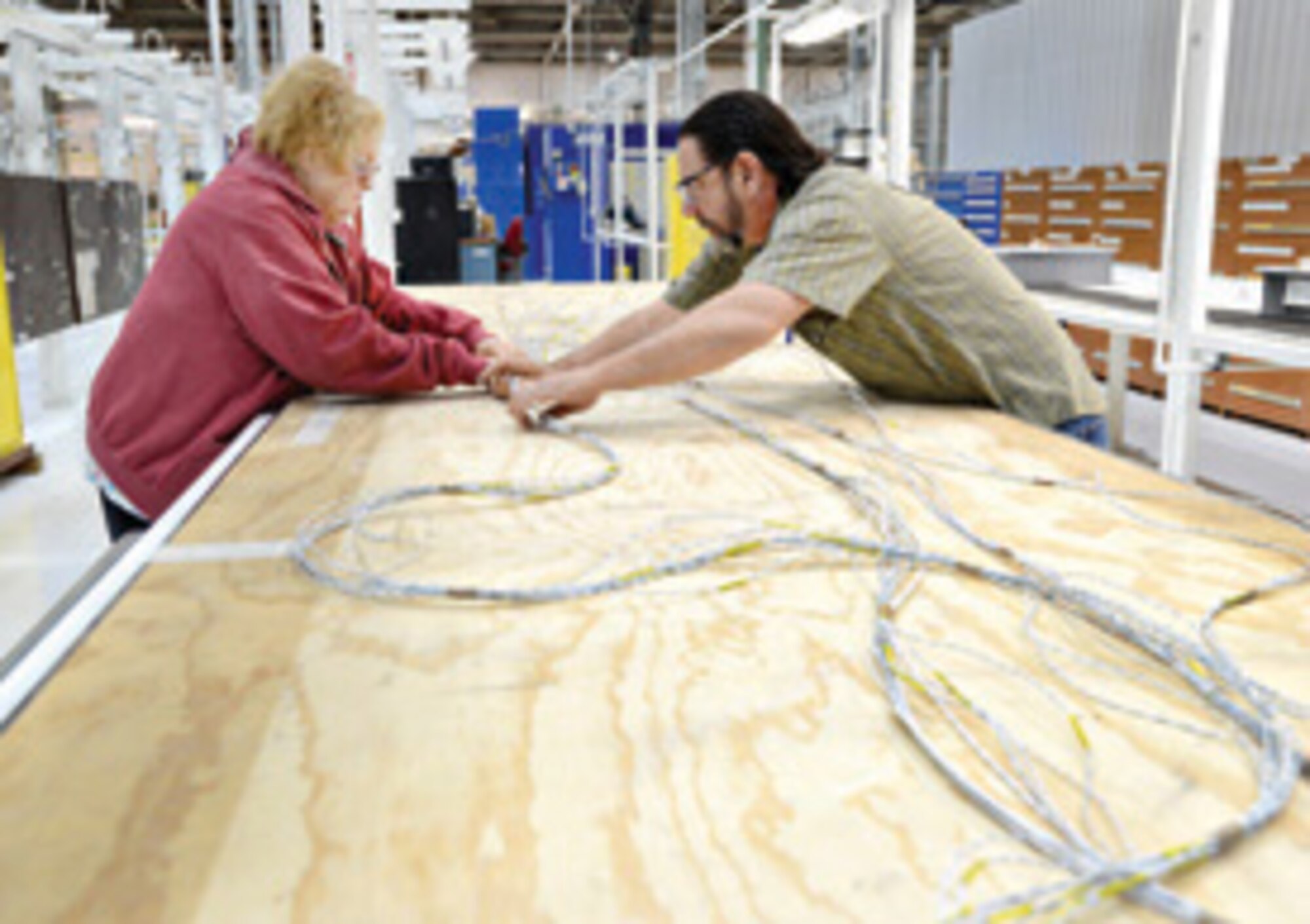 Linda Burrows, with the 552nd Commodities Maintenance Group’s cable harness shop, and Donald Califf, with the 567th Aircraft Maintenance Squadron’s Maintenance Repair Overhaul Technology Center, work together to reformat a wire harness into connectors. The harness is built in the cable harness shop and then installed at the MROTC.  Air Force photo by Kelly White/Released