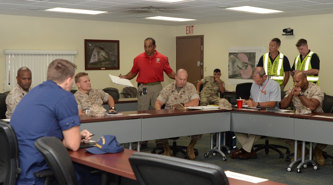 Fred Rogers (standing, center), installation emergency manager/CBRNE protection officer, Mission Assurance Branch, Blount Island Command, briefs Col. Brian Hughes, commanding officer, BICmd, Marine Corps Support Facility Blount Island, Jacksonville, Fla., after a mock bomb-threat exercise on the installation, recently. Officials aboard BICmd participated in the full-scale exercise to test the effectiveness of procedures in the event an actual bomb threat or other emergency is reported.
