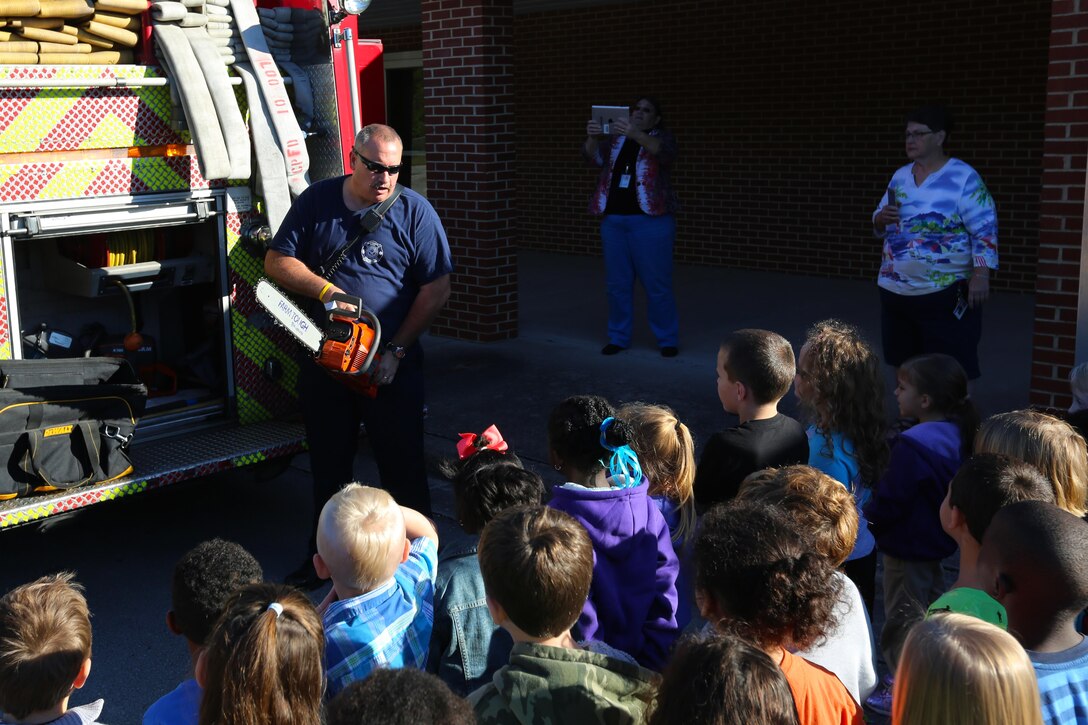 Dickie Thomas showcases gear used on a firetruck during a visit to W. J. Gurganus Elementary School is Havelock, N.C., Oct. 22, 2015. Members of the Marine Corps Air Station Cherry Point Fire and Emergency Services Department visited the local elementary school to teach children about the importance of fire safety and prevention. The air station fire department actively participates in school visits to encourage children of all ages to practice safety measures to keep both their families and themselves safe. Thomas is a fire captain with the MCAS Cherry Point Fire and Emergency Services Department. (U.S. Marine Corps photo by Cpl. N.W. Huertas/Released)