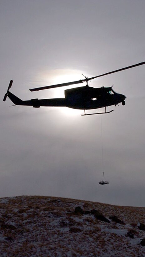 The silhouette of a UH-1N Huey helicopter from the 40th Helicopter Squadron hovers over the Montana skyline near the Rocky Mountain Front during a search and rescue training sortie Nov. 19. The stokes litter, a stretcher designed to transport people from the ground to the helicopter while in the air, is slowly lowered by the on-board flight engineer for a simulated search and recovery mission. (U.S. Air Force photo/Senior Airman Eydie Sakura).                         
