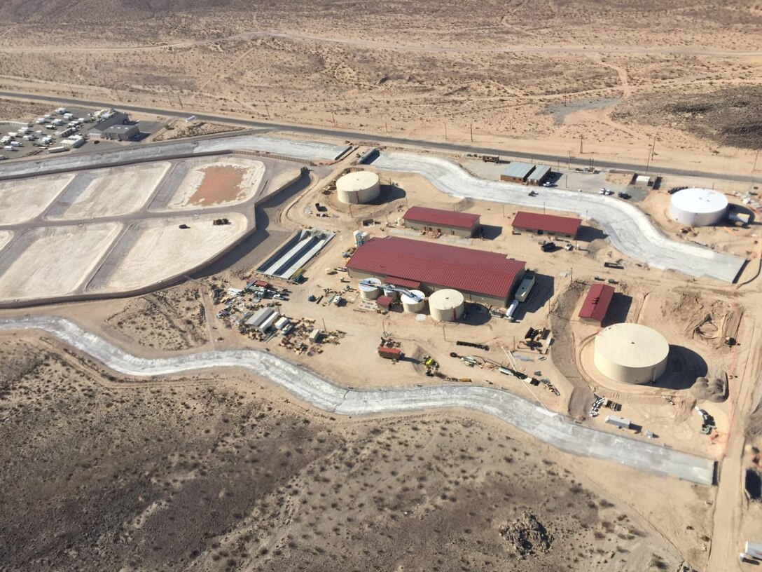 Aerial view of Fort Irwin’s new water treatment Plant (Courtesy photo provided Sgt. Maj. (RET) Scott Blum)
The plant (red roofs and four water tanks) is the main purification system of the water treatment plant. The concrete channels around the plant are built to safeguard the plant from storm water events and also provides full containment of the plants processing water in case of catastrophic failure of the plant. The ponds shown on the top of the photo are the evaporation ponds to handle less than 1% of the brine water remnants from the water treatment system.

The project is the design-build of a six million gallon per day water treatment plant. The new plant will use a three-stage, electro-dialysis reversal (EDR) water treatment plant that treats all contaminants found in Fort Irwin's ground water in accordance with federal and state requirements.
The plant will include: an electro-dialysis reversal (EDR) primary treatment, lime softening clarifiers, lime solids thickeners, lime sludge lagoons, reverse osmosis (RO) filters, brine treatment facility, concentrate equalization basins and a mechanical evaporator tower and feed tank, and three evaporation ponds to achieve the post’s 99 percent water recovery rate.
The project also includes water system improvement and supporting utilities and infrastructure upgrades
