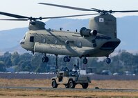 Airmen from the 60th Aerial Port Squadron and the Army National Guard's 49th Police Brigade practice loading and sling loading vehicles on a CH-47 Chinook cargo helicopter Oct. 14, 2015, at Travis Air Force Base, California. The units also practiced night time operations in total darkness with the aid of night vision goggles. (U.S. Air Force photo by T.C. Perkins Jr.)