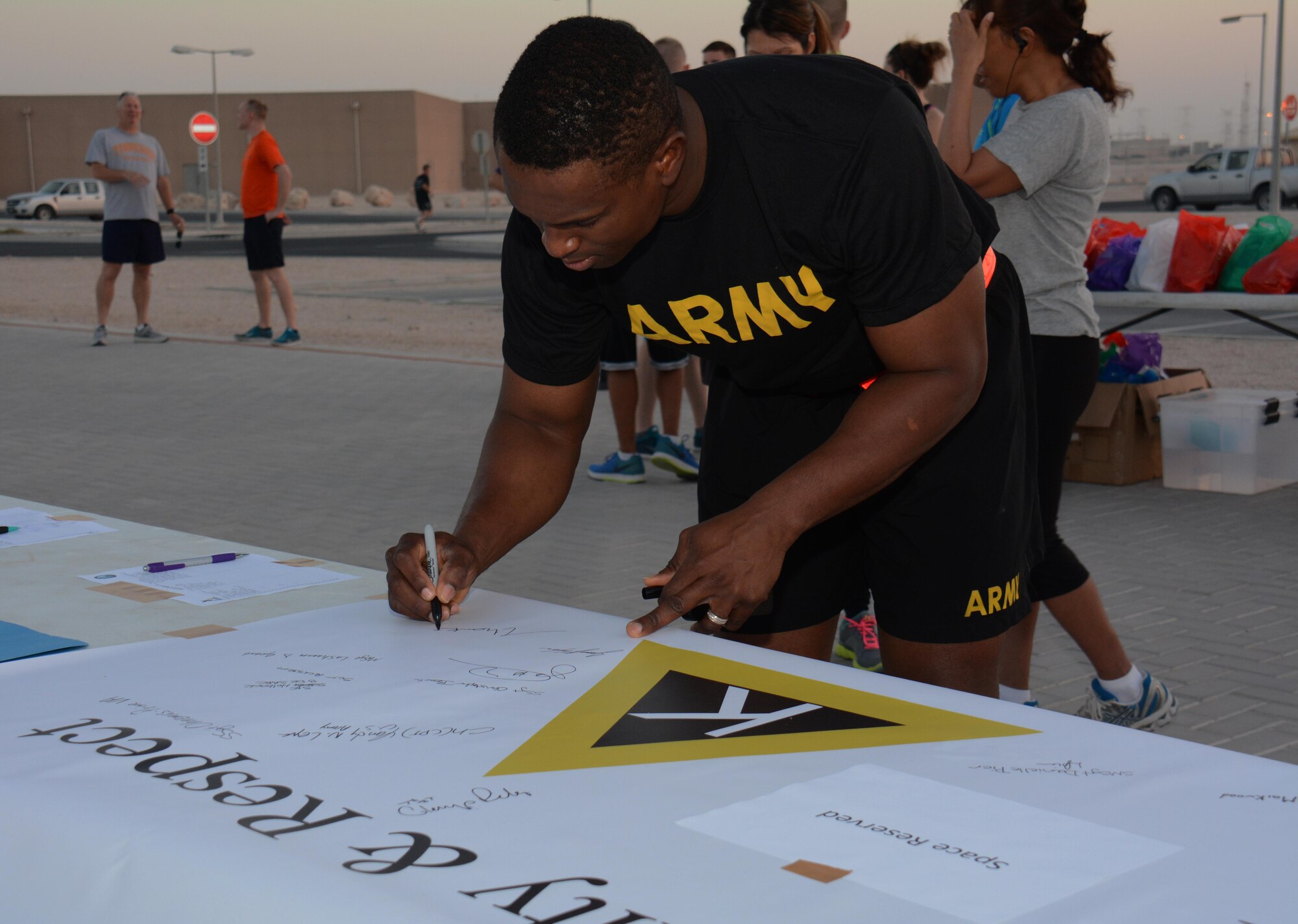 U.S. Army Capt. Maxwell Babjide, 31st Air Defense Artillery Brigade, signs a pledge to treat people with respect Oct. 23, 2015 at the Dignity and Respect 5K at Al Udeid Air Base, Qatar. Babjide joined more than 150 other runners to take part in the 3.1 mile race. (U.S. Air Force photo/Tech. Sgt. James Hodgman/Released)