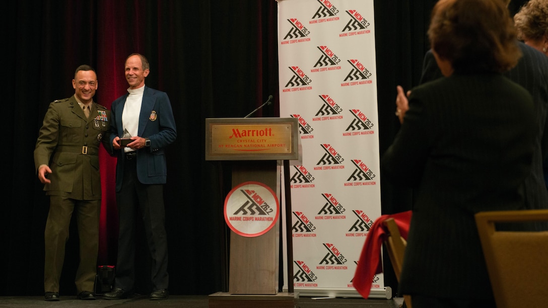 Col. Joseph M. Murray, commander, Marine Corps Installations National Capital Region-Marine Corps Base Quantico, presents Jeff Galloway with a plaque during a Marine Corps Hall of Fame dinner and ceremony at the Hyatt Regency Reagan National Airport in Crystal City, Va., Oct. 23, 2015. Galloway was inducted into the Marine Corps Marathon Hall of Fame for his contributions to the marathon over the years. Galloway, a retired Navy lieutenant and founder of the Run-Walk-Run program, has been involved with the marathon for 20 years and has completed 12. He travels the nation hosting running clinics and encouraging runners to be safer and easier on their bodies.