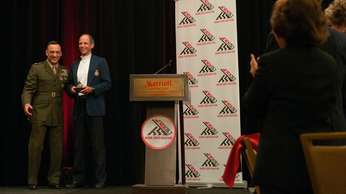 Col. Joseph M. Murray, commander, Marine Corps Installations National Capital Region-Marine Corps Base Quantico, presents Jeff Galloway with a plaque during a Marine Corps Hall of Fame dinner and ceremony at the Hyatt Regency Reagan National Airport in Crystal City, Va., Oct. 23, 2015. Galloway was inducted into the Marine Corps Marathon Hall of Fame for his contributions to the marathon over the years. Galloway, a retired Navy lieutenant and founder of the Run-Walk-Run program, has been involved with the marathon for 20 years and has completed 12. He travels the nation hosting running clinics and encouraging runners to be safer and easier on their bodies.