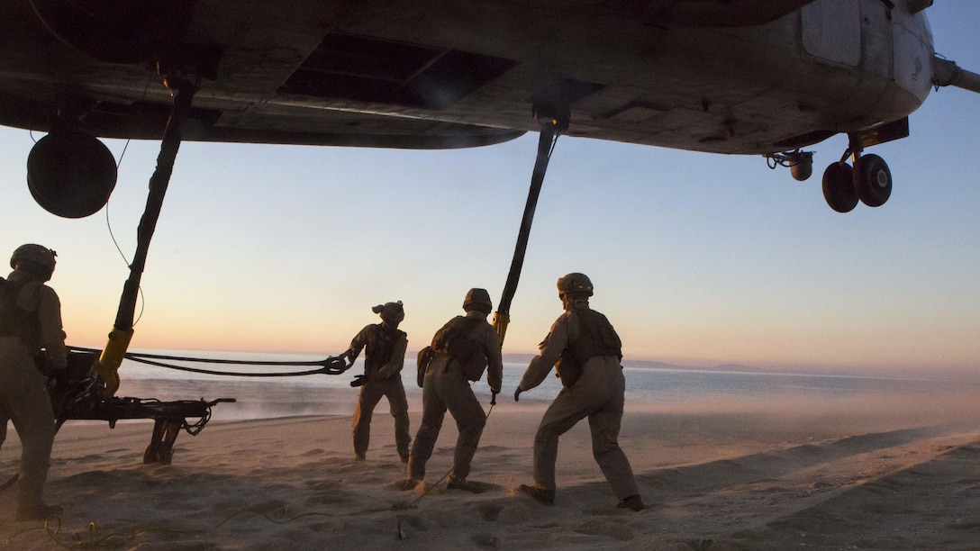 U.S. Marines with the Helicopter Support Team, Landing Support Detachment with the 26th Marine Expeditionary Unit, embarked aboard the amphibious transport dock ship USS Arlington (LPD 24) prepare to attach a sling connected to a M105 trailer to a lifting hook from a CH-53E Super Stallion with Marine Medium Tiltrotor Squadron (VMM) 162 (Reinforced), 26th MEU, hovering overhead during an external lift training exercise at Pinheiro Da Cruz, Praia Da Raposa Beach, Portugal, Oct. 22, 2015, during Trident Juncture 15. Trident Juncture is a NATO-led exercise designed to certify NATO response forces and develop interoperability among participating NATO and partner nations. 