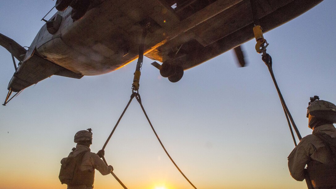 U.S. Marine Lance Cpl. James Stamper (left) and Lance Cpl. James Stamper (right), landing support specialists, with the Landing Support Detachment, 26th Marine Expeditionary Unit embarked aboard the amphibious transport dock ship USS Arlington (LPD 24), hold slings connecting the M105 trailer to a CH-53E Super Stallion with Marine Medium Tiltrotor Squadron (VMM) 162 (Reinforced) at Pinheiro Da Cruz, Praia Da Raposa Beach, Portugal, Oct. 22, 2015, during Trident Juncture 15. Trident Juncture is a NATO-led exercise designed to certify NATO response forces and develop interoperability among participating NATO and partner nations. 