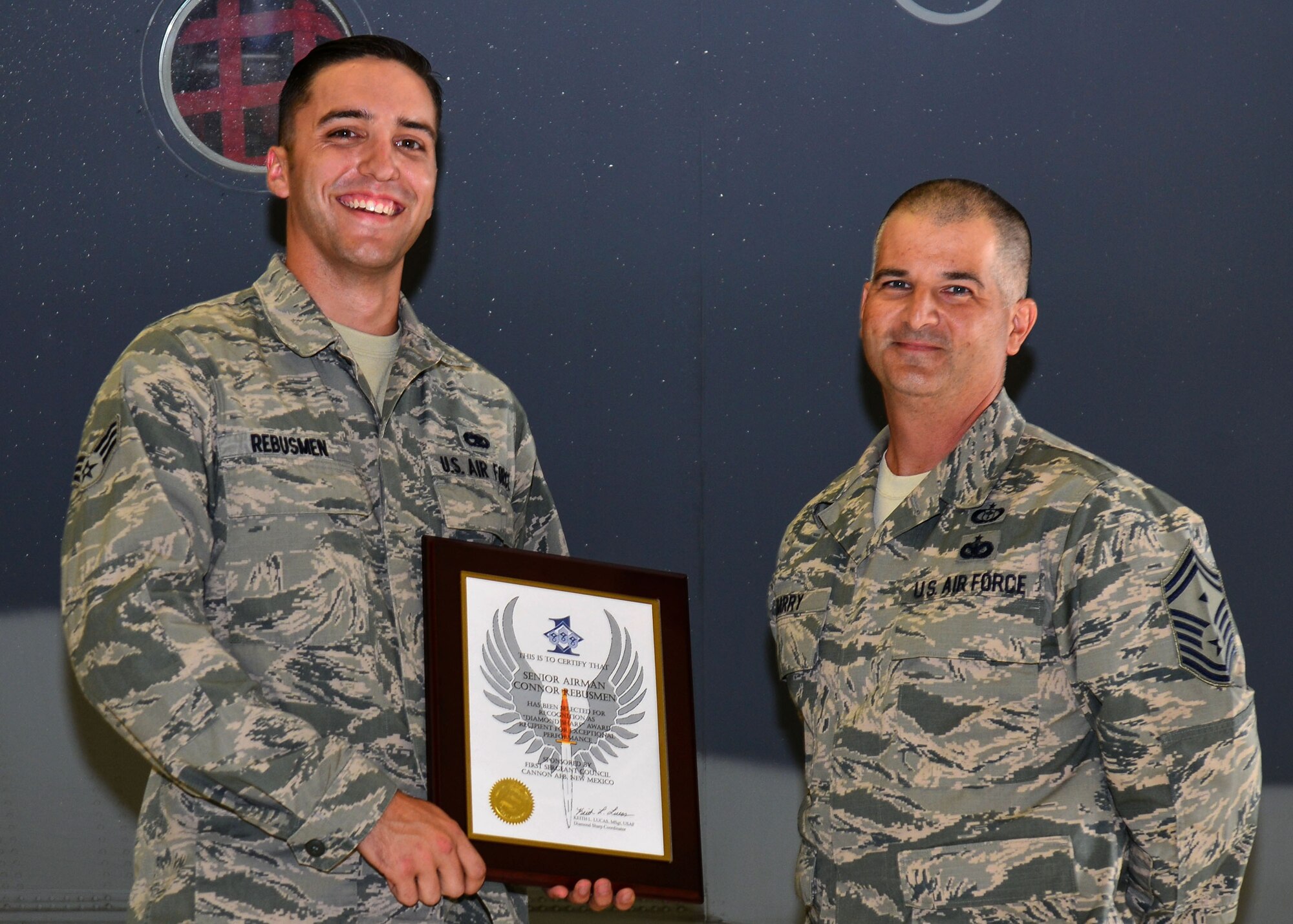 U.S. Air Force Senior Airman Connor Rebusmen, 27th Special Operations Aircraft Maintenance Squadron crew chief, stands with Senior Master Sgt. Bill Barry, 27th SOAMXS first sergeant, during his Diamond Sharp Award recognition Aug. 14, 2015, at Cannon Air Force Base, N.M. Rebusmen is an MC-130J crew chief assigned to the 9th Aircraft Maintenance Unit, who spends ample time setting the bar for community involvement within his squadron. (U.S. Air Force photo/Airman 1st Class Shelby Kay-Fantozzi) 