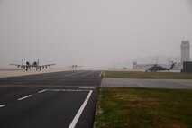 Two U.S. Air Force A-10 Thunderbolt IIs from the 25th Fighter Squadron taxi along the runway of Osan Air Base, Republic of Korea, Oct. 16, 2015, while an HH-60 Pavehawk assigned to the 33rd Rescue Squadron from Kadena Air Base, Japan is prepped for take-off. The squadrons are participating in the combat search and rescue exercise, Exercise Pacific Thunder 15-02. (U.S. Air Force photo by Staff Sgt. Benjamin Sutton/Released)