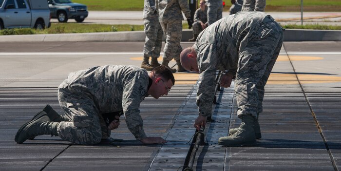 (From left to right) 628th Civil Engineering Squadron operators SSgt. Christopher Spann and SSgt. Christopher Gentry finish resetting the aircraft arresting system on the flight line after being tested by an F-16 Fighting Falcon from Shaw Air Force Base, S.C., at Joint Base Charleston – AB, S.C., on Oct. 14, 2015. The AAS is used on U.S. Navy aircraft carriers and JB Charleston is one of a few land bases that have the AAS installed. (U.S. Air Force photo/Airman 1st Class Thomas T. Charlton)
